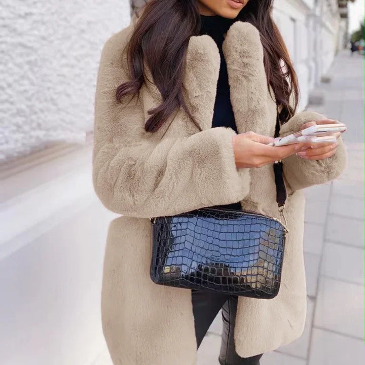 Woman wearing beige faux fur coat with black crocodile leather crossbody bag holding smartphone