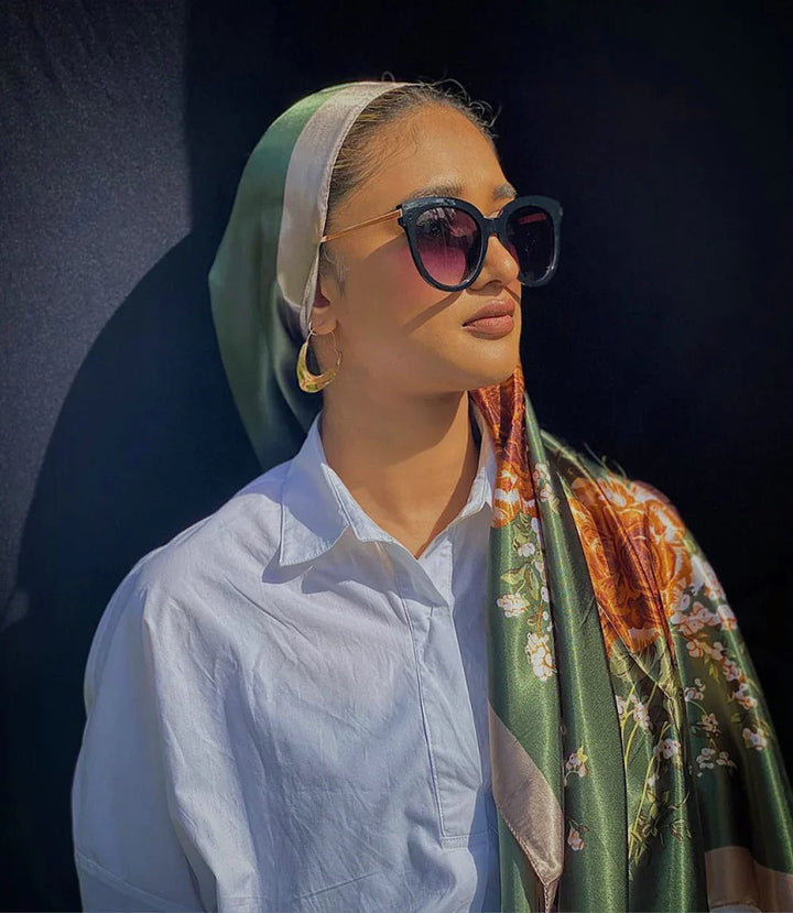 Woman wearing floral silk scarf, white shirt, oversized sunglasses, and gold hoop earrings against dark background