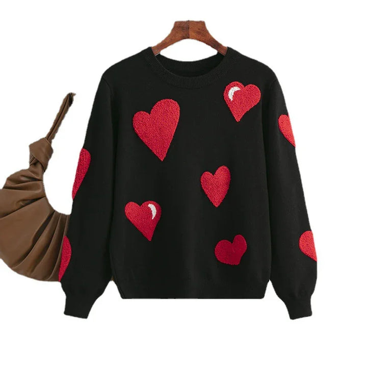 Black sweater with red heart patterns on front and sleeves displayed on wooden hanger with brown bag