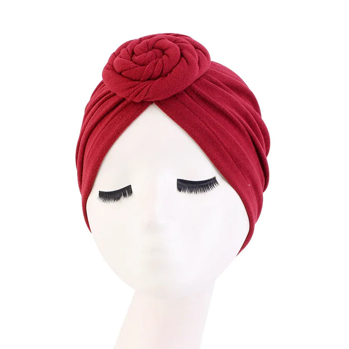 Red turban headwrap with rose knot detail on white mannequin head with long eyelashes