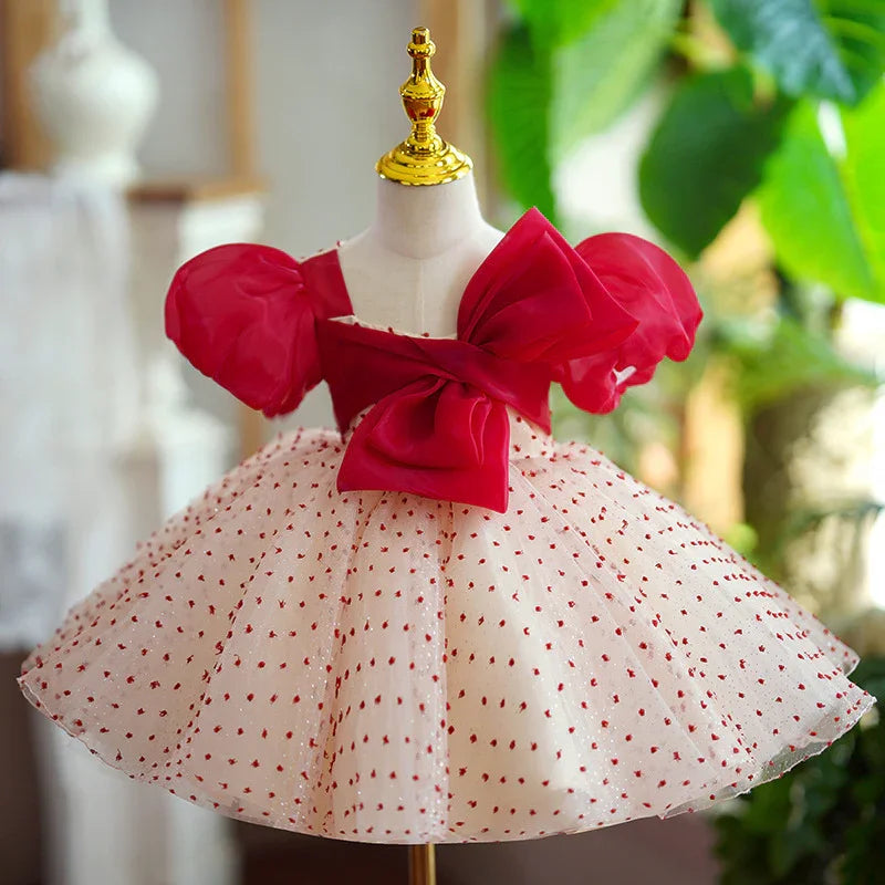 Elegant baby dress with red puff sleeves, large bow, and white tulle skirt with red dots on mannequin