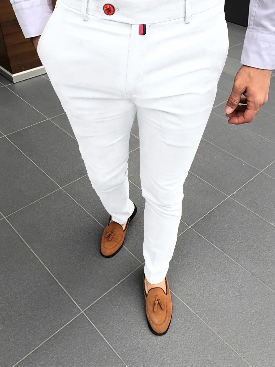 Man wearing slim fit white pants and brown tassel loafers standing on gray tiled floor