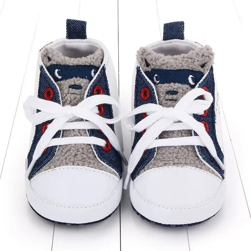 Baby shoes with white toes, navy side panels, red eyelets, white laces, and gray fuzzy interior lining