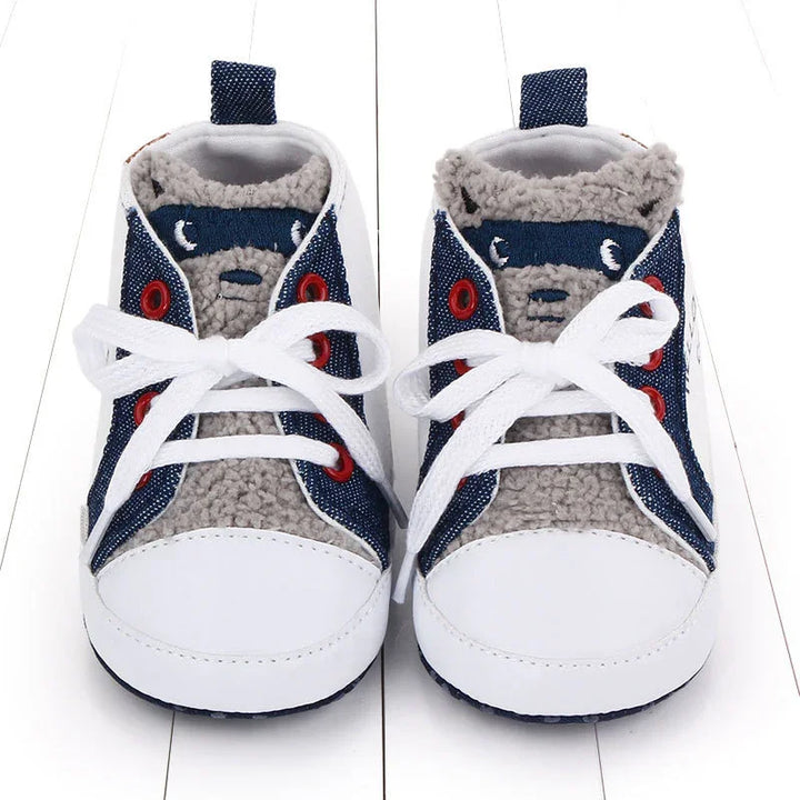 Baby shoes with white toes, navy side panels, red eyelets, white laces, and gray fuzzy interior lining