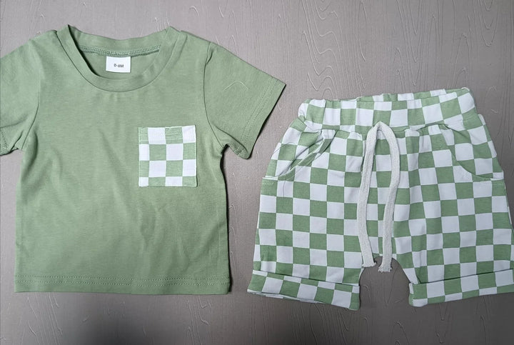 Green baby T-shirt with white and green checkered pocket and matching checkered shorts on grey surface