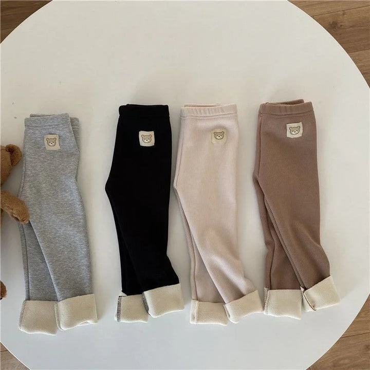 Four pairs of children's ribbed leggings in gray, black, cream, and brown with bear patch and cuffed ankles