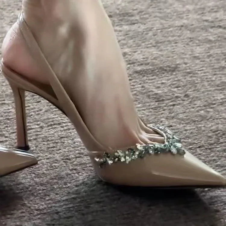 Beige high heel slingback shoe with jeweled embellishments on toe worn on carpeted floor