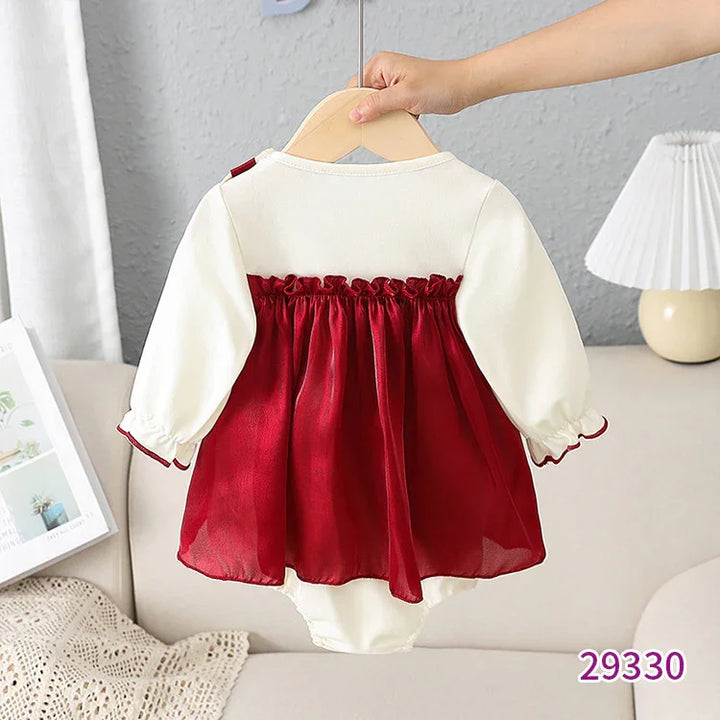 Baby dress with long white sleeves and red ruffled skirt hanging on wooden hanger indoors