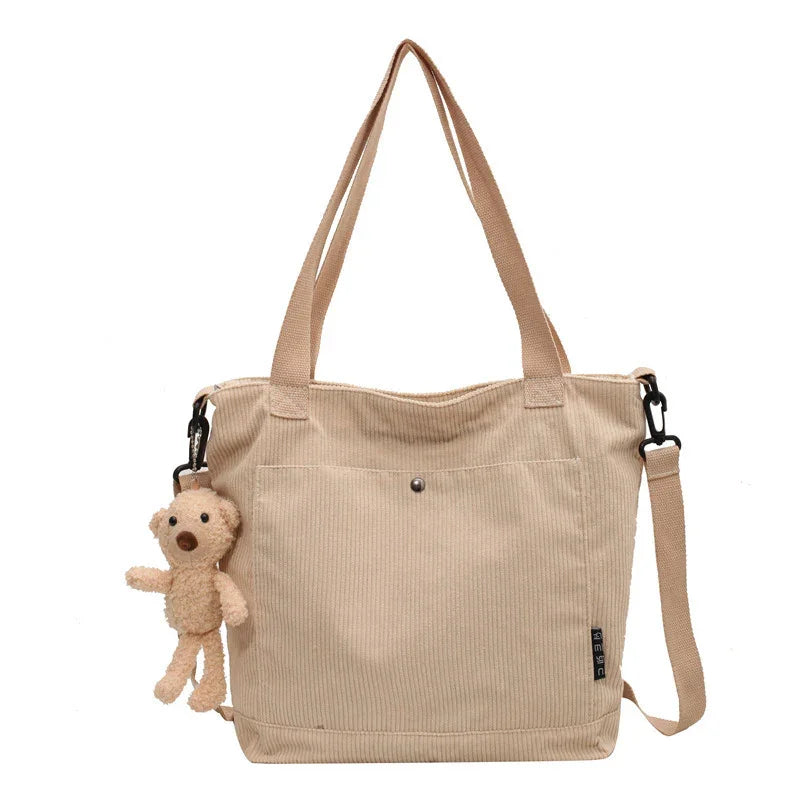 Beige corduroy tote bag with front pocket, shoulder strap, and small plush teddy bear charm