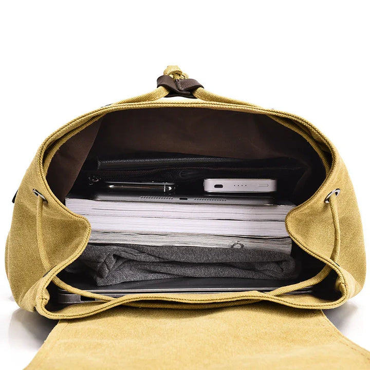 Open mustard yellow canvas backpack with books, gray clothing, tablet, and portable charger inside