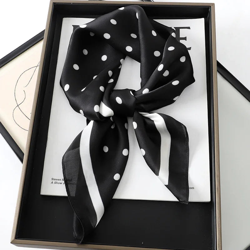 Black silk scarf with white polka dots and stripes placed in a box on white paper