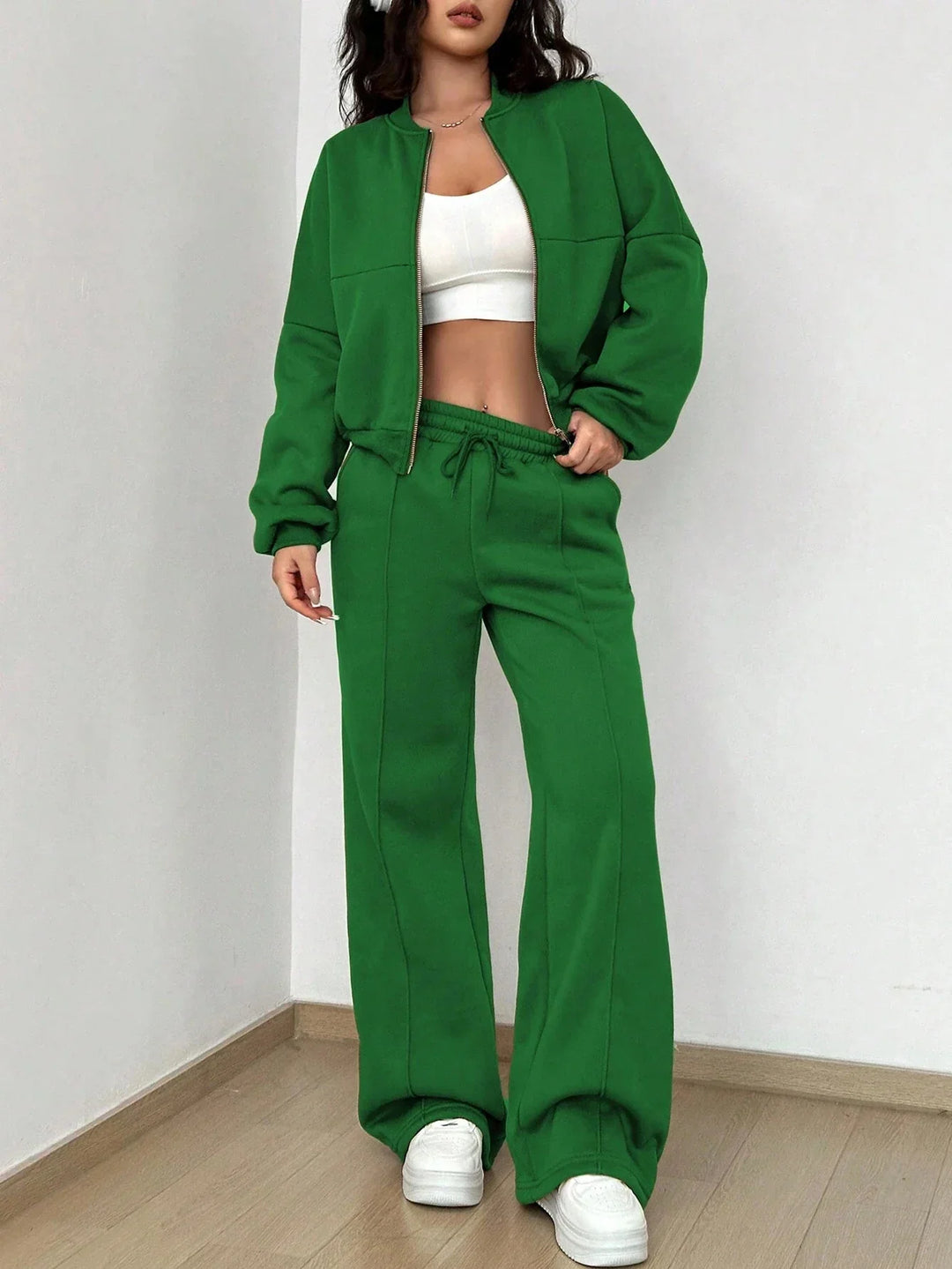 Woman wearing green zip-up jacket and matching wide-leg pants with white crop top and sneakers