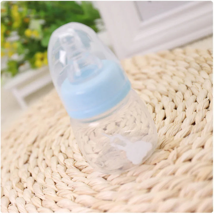 Clear baby bottle with blue cap on woven mat near green and yellow blurred background