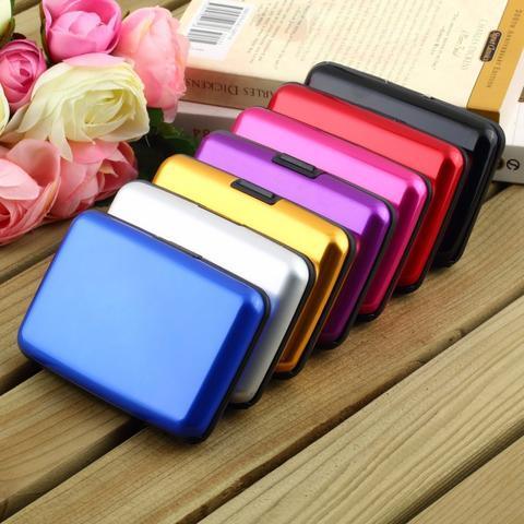 Colorful metal card holders in blue, silver, gold, purple, pink, red, and black on wooden surface with roses and books