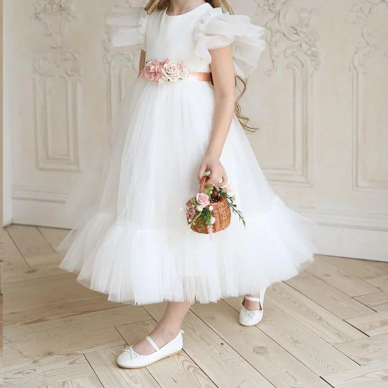 Girl wearing white tulle dress with floral waist belt holding small wicker basket with flowers