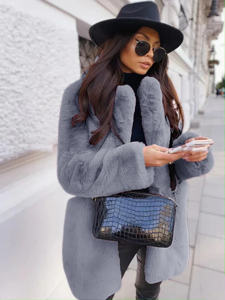 Woman wearing a gray faux fur coat, black wide-brim hat, sunglasses, and holding a black crocodile leather handbag on city street