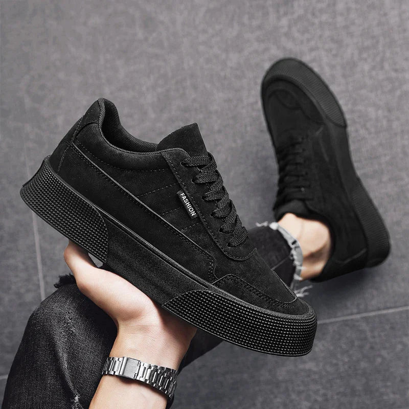 Black casual sneakers with textured soles, worn with dark jeans on gray tiled floor