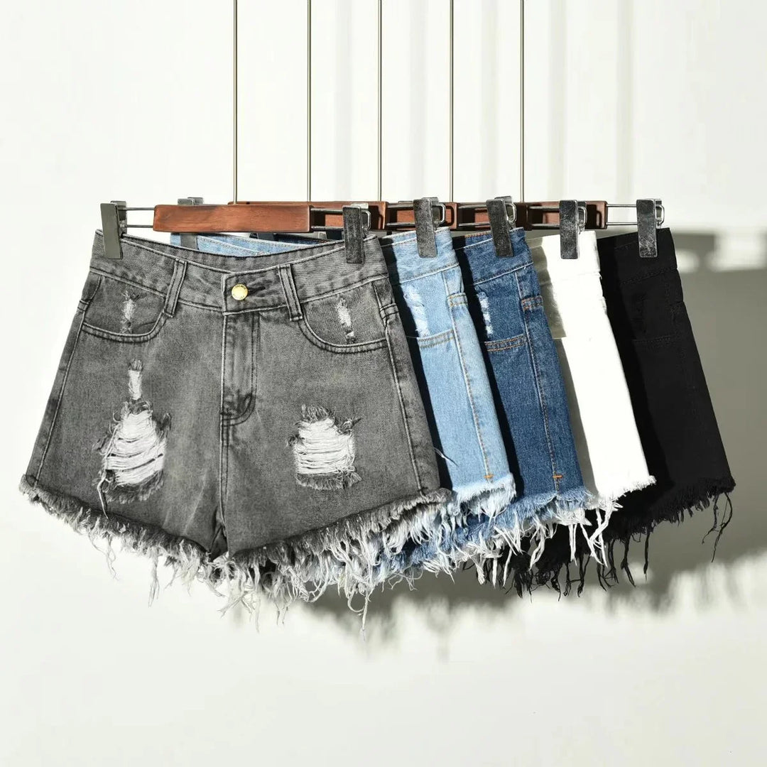 Five pairs of distressed denim shorts in gray, light blue, blue, white, and black hanging on wooden hangers