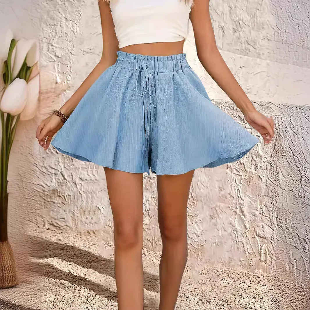 Woman wearing light blue loose fit shorts with drawstring waist and white crop top in textured indoor setting
