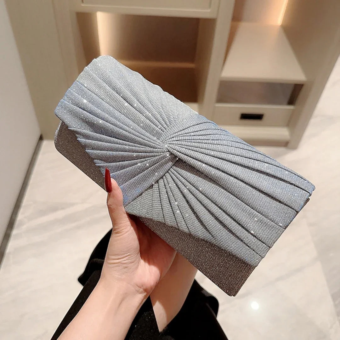 Hand holding a silver pleated evening clutch bag with metallic shimmer in a modern interior