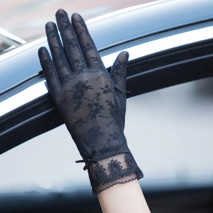 Hand wearing elegant black lace gloves with floral pattern and scalloped wrist detail over car window