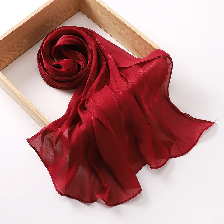 Elegant sheer red chiffon scarf rolled inside a wooden frame on white background