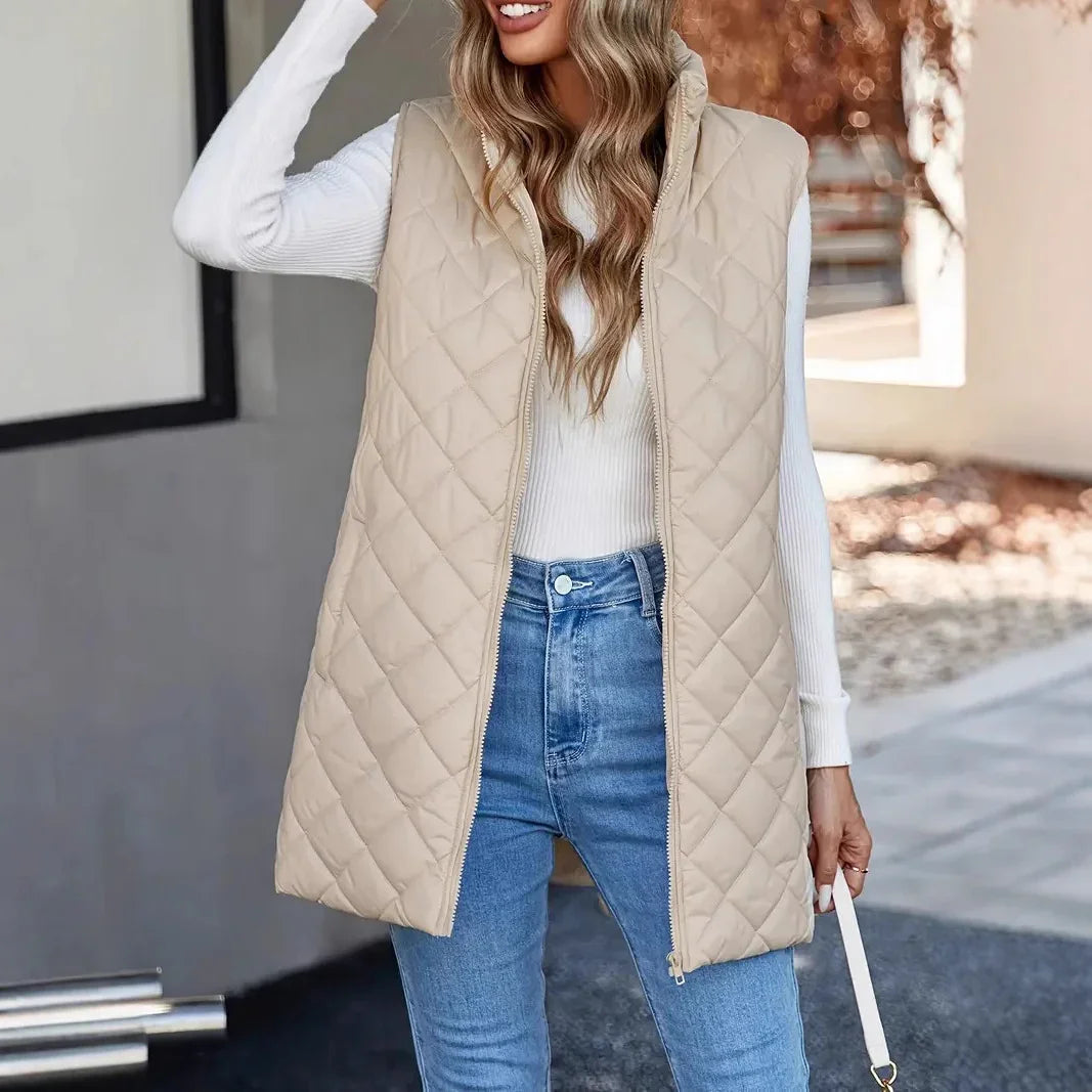 Woman wearing beige quilted sleeveless vest over white ribbed sweater and blue jeans in outdoor setting