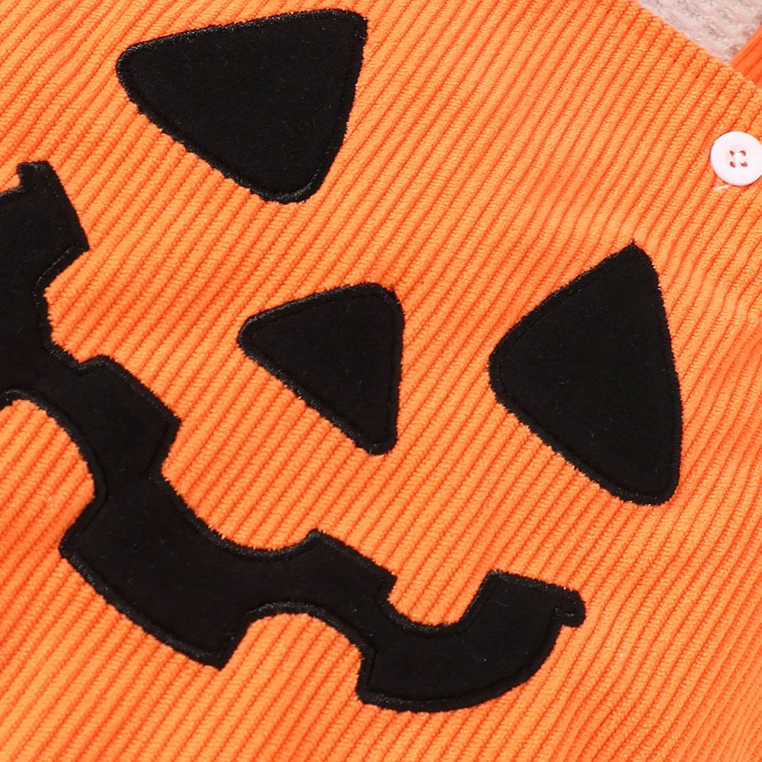 Close-up of orange corduroy fabric with stitched black jack-o'-lantern face design and a white button
