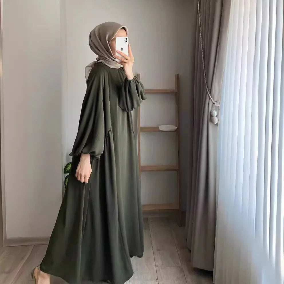 Woman wearing olive green modest maxi dress and beige hijab taking mirror selfie in minimal room