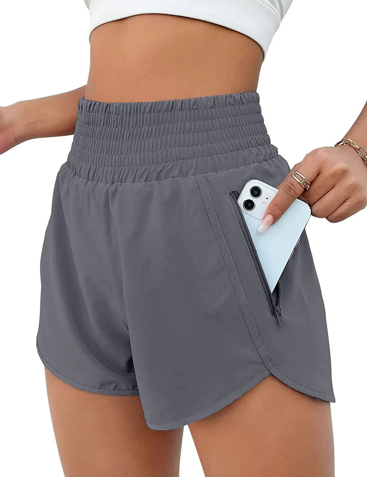 Close-up of woman wearing gray high-waisted athletic shorts with zippered pocket holding smartphone