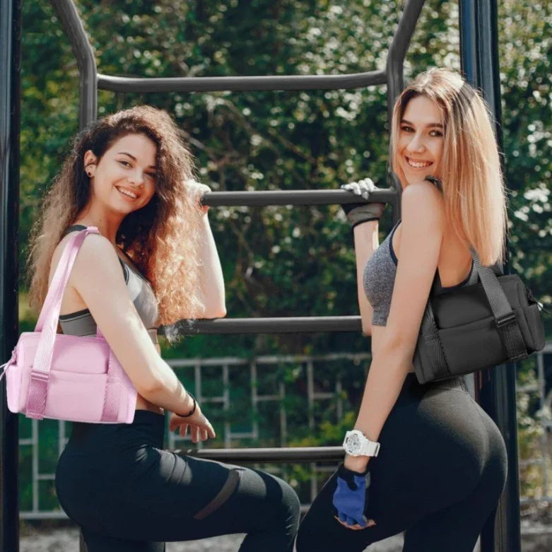 Two fit women in sportswear with pink and black gym bags posing on outdoor fitness bars under sunlight