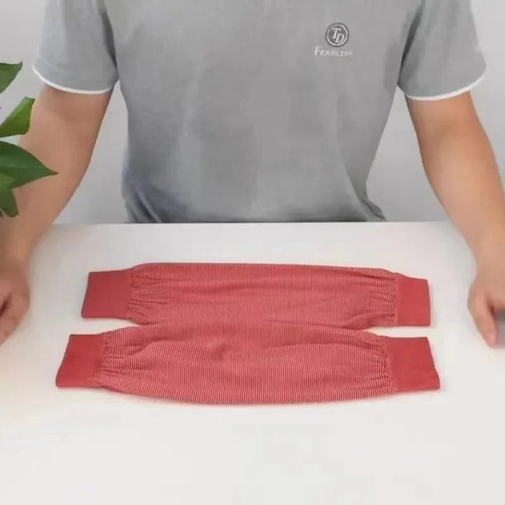 Person in gray t-shirt presenting two red stretchy arm sleeves on a white table with green plant visible
