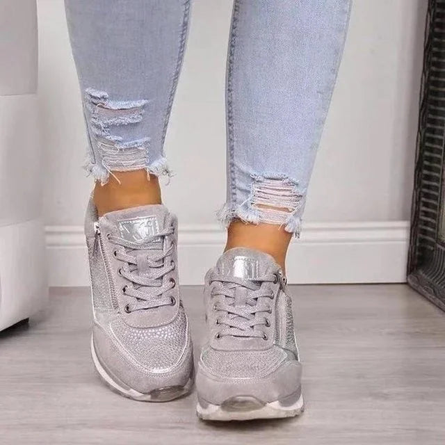 Woman wearing light gray sneakers with textured detailing and light blue ripped skinny jeans on gray floor