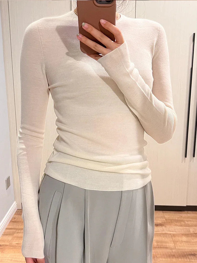 Person wearing a fitted long-sleeve beige sweater and light gray pleated pants taking a mirror selfie