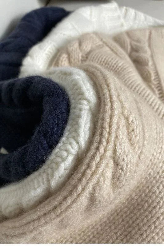 Close-up of folded knit sweaters in beige, white, and navy blue with cable knit details