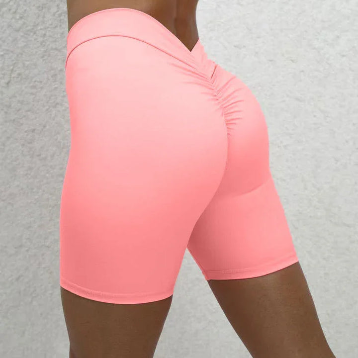 Close-up of woman wearing coral pink high-waisted ruched biker shorts against light gray background