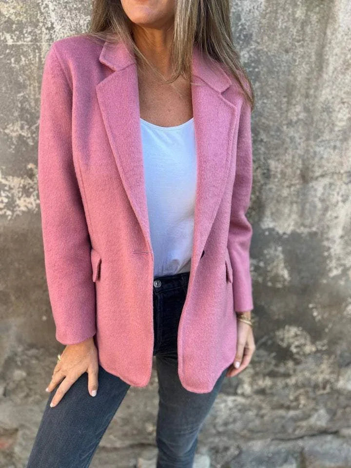 Woman wearing a pink wool blazer over a white top and dark jeans against a textured stone wall