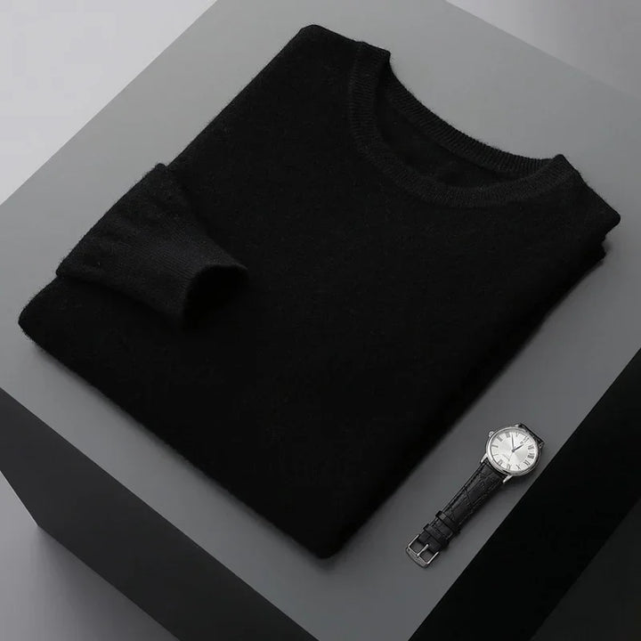 Folded black sweater on gray platform next to a silver wristwatch with black leather strap