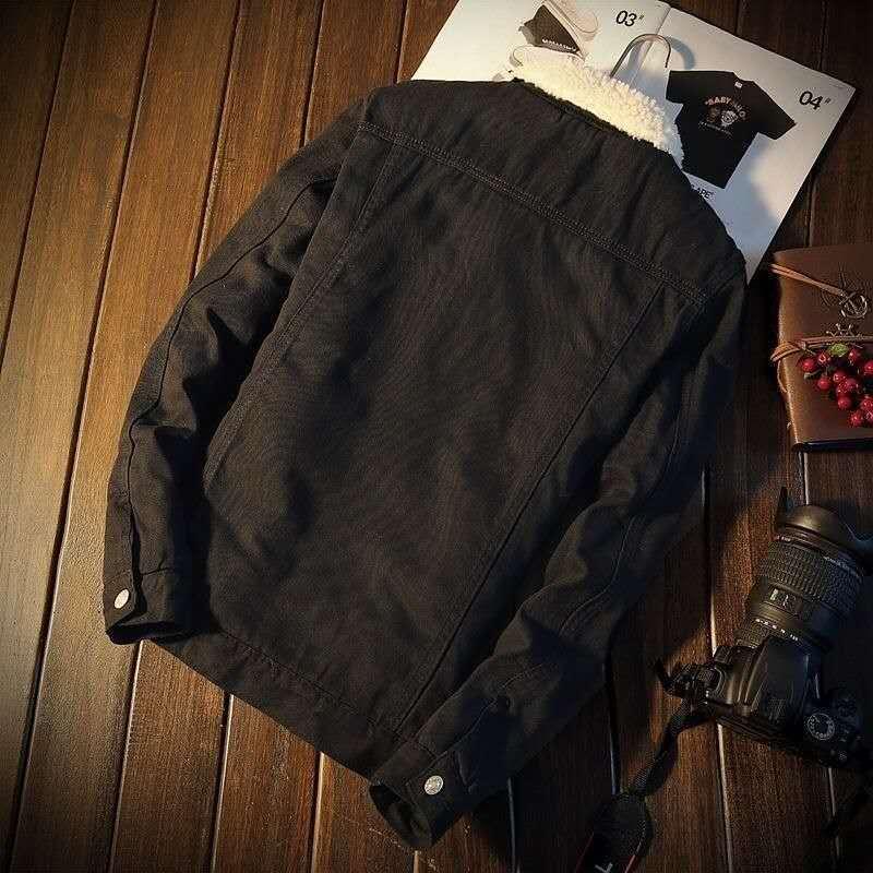 Black denim jacket with white sherpa collar on wooden floor next to camera and notebook