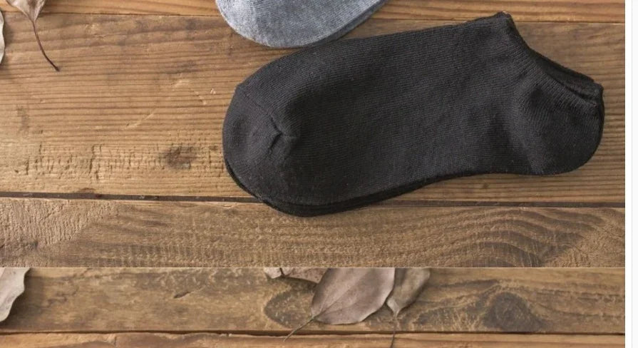Pair of black and gray ankle socks on wooden surface with autumn leaves