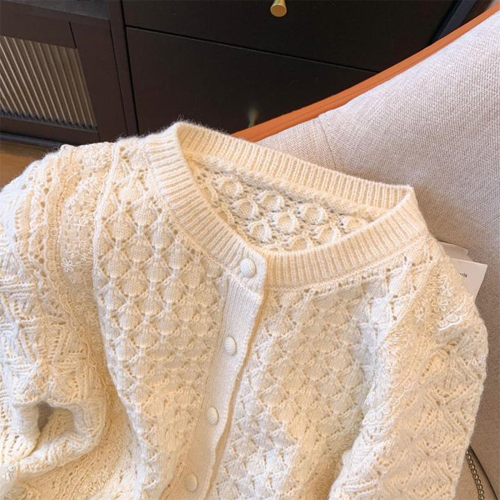 Cream knit cardigan with textured cable and floral patterns laid on beige fabric