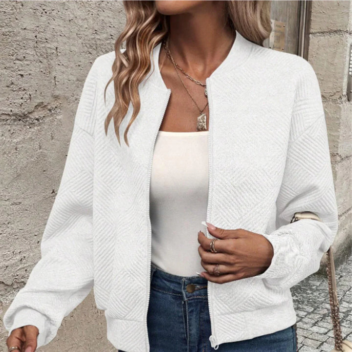 Woman wearing white textured knit bomber jacket with zipper over white top and blue jeans