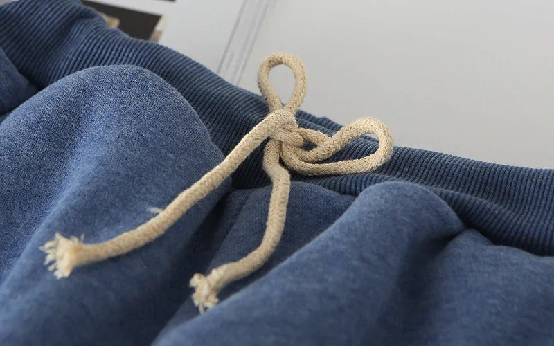 Close-up of blue sweatpants with beige drawstring knot and ribbed waistband fabric