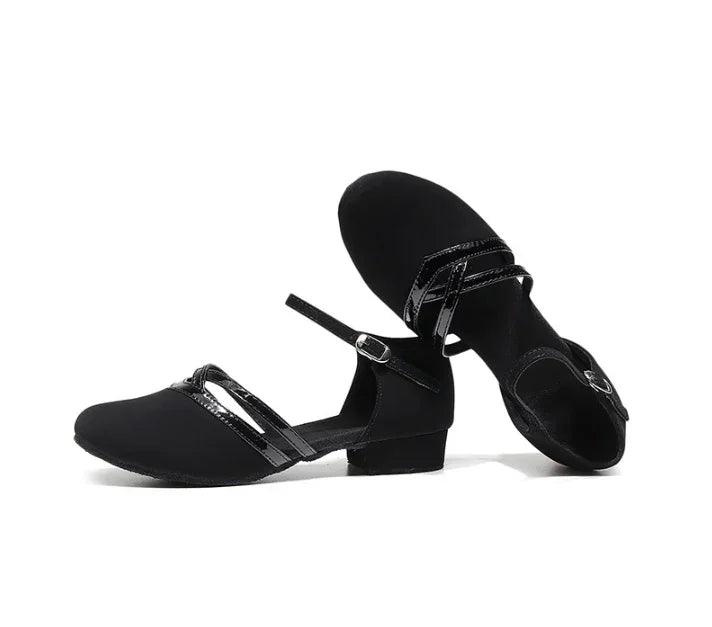 Black women's dance shoes with low heels and glossy cross straps on white background