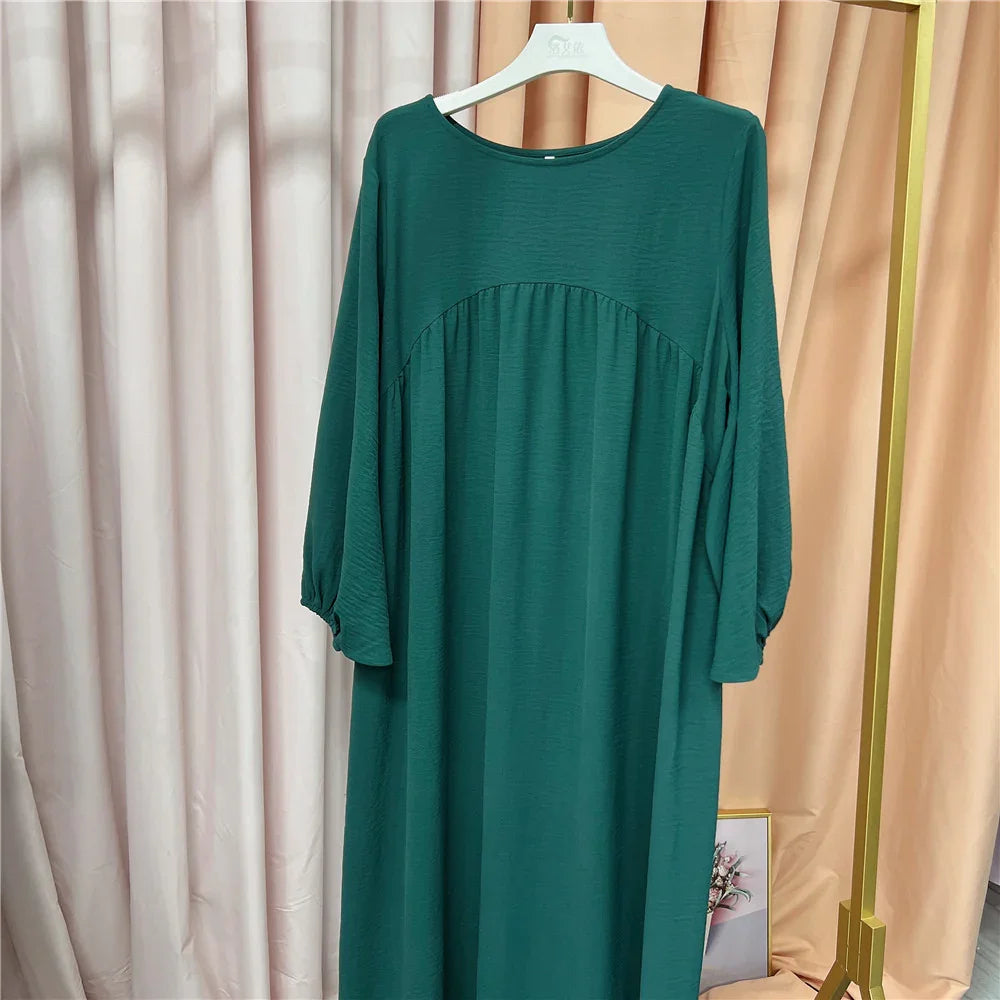 Dark green long sleeve loose dress hanging on white hanger with beige and cream curtains background