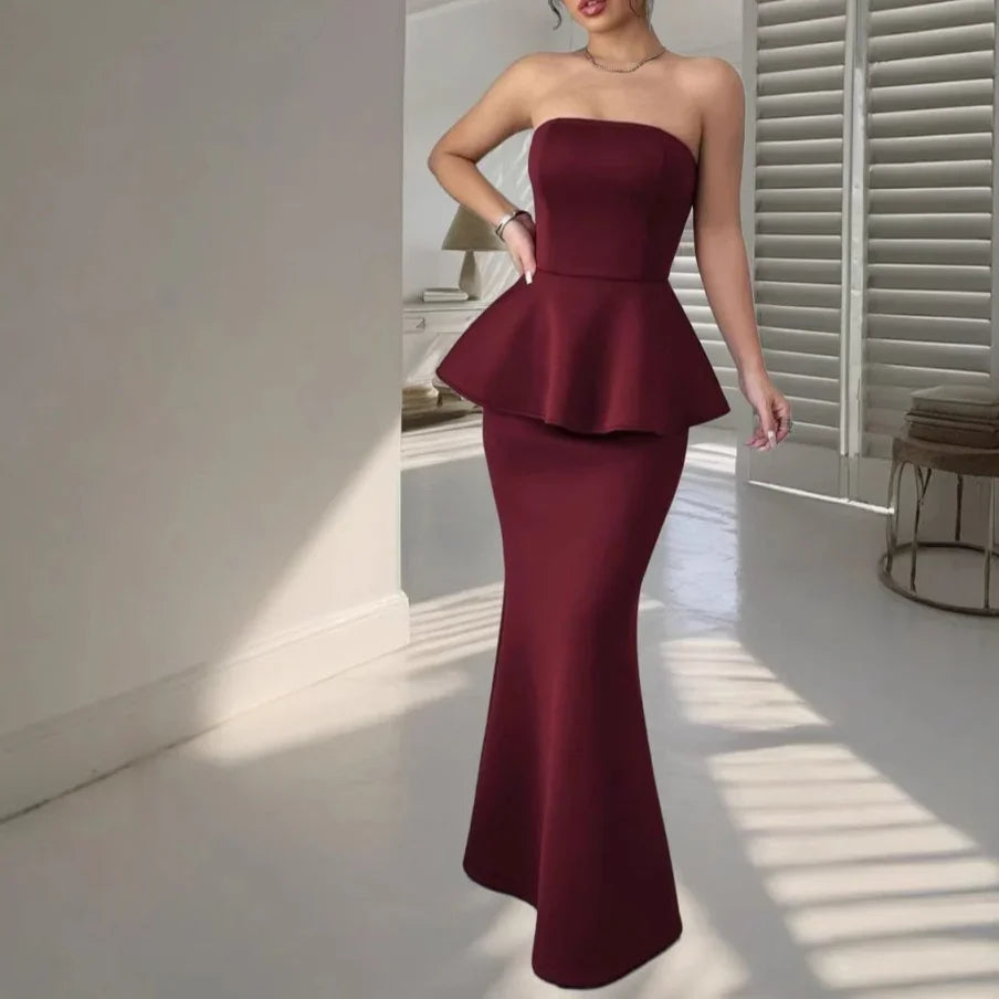 Woman in elegant strapless burgundy peplum mermaid evening gown in minimalist white room