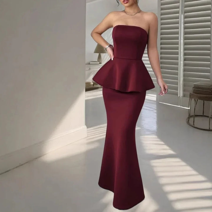 Woman in elegant strapless burgundy peplum mermaid evening gown in minimalist white room
