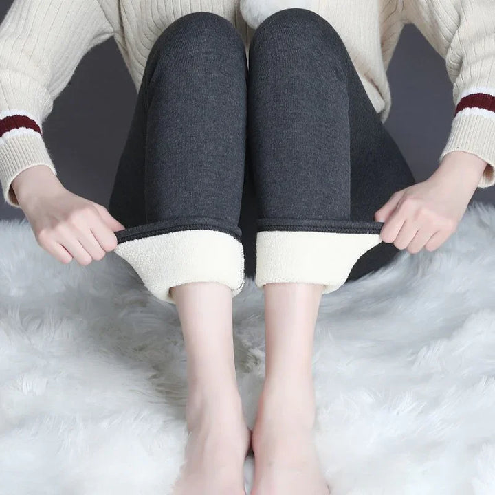 Woman wearing dark gray fleece-lined leggings with cuffs rolled up, sitting on white fluffy rug