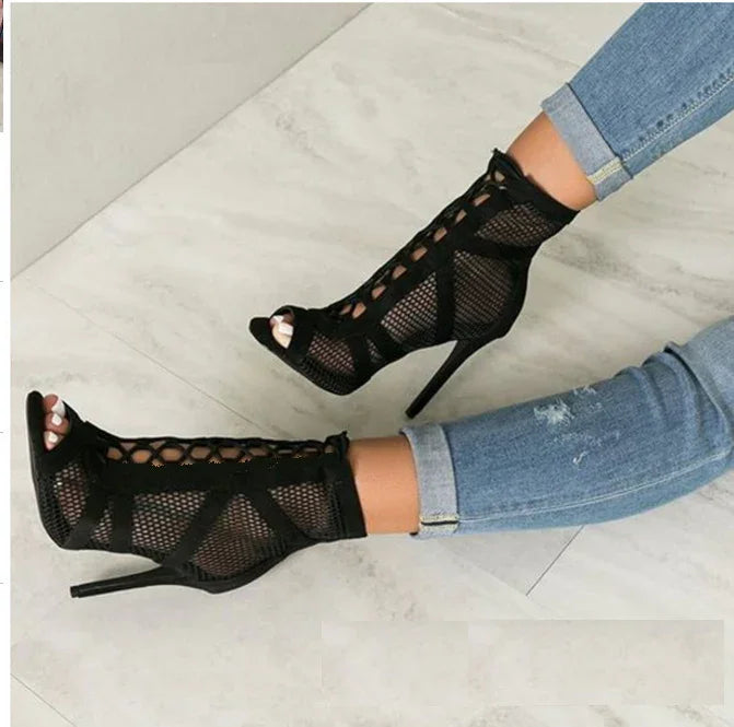 Black mesh stiletto ankle boots with lace-up details worn with rolled-up blue jeans on tiled floor