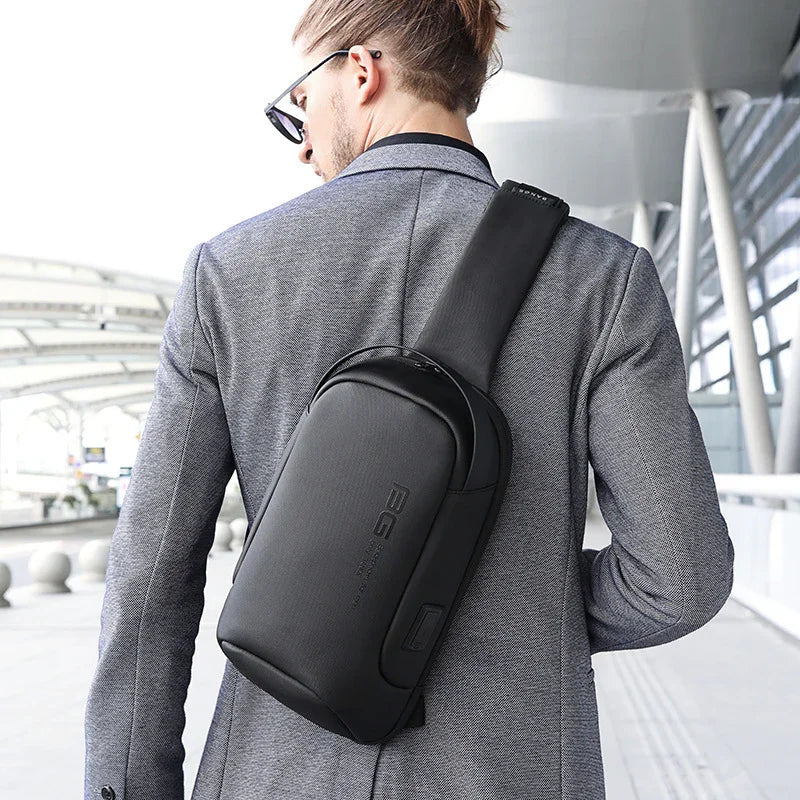 Man wearing sunglasses and gray blazer with black crossbody sling backpack in urban modern setting